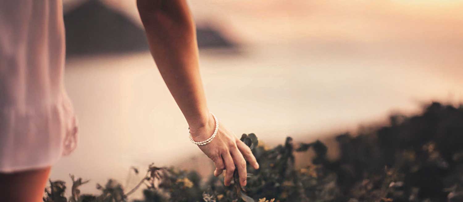 Woman's arm with a diamond bracelet, fingers brushing against greenery | Physis Publishing | Quietly Iconic Brands