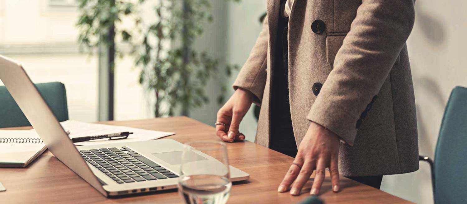 A woman standing at her desk, fingertips resting on the surface | Physis Publishing | Quietly Iconic Brands